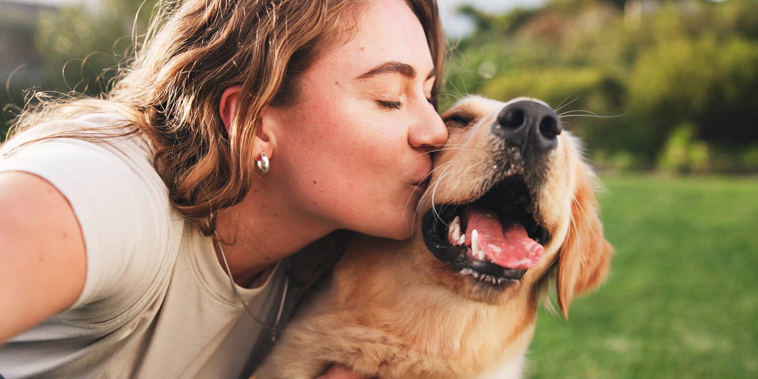 woman outside kissing her golden retriever